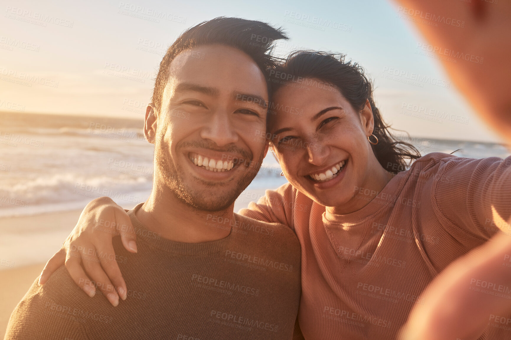 Buy stock photo Portrait of a young diverse biracial couple taking a selfie at the beach and having fun outside