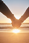 Closeup shot of two people holding hands at the beach at sunset