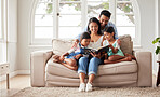Young happy family sitting on the sofa and reading a book together at home while relaxing