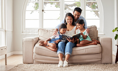 Buy stock photo Shot of a young couple reading a book to their daughters while sitting on a sofa at home