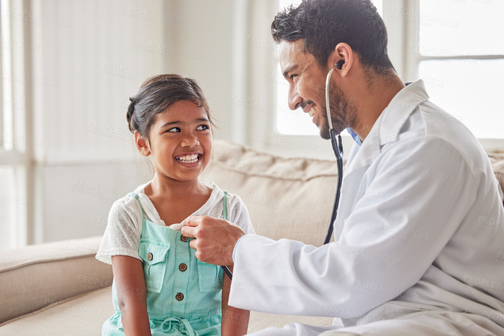 Buy stock photo Young handsome smiling doctor using a stethoscope to listen to a sick little girls heartbeat during a house call checkup at home