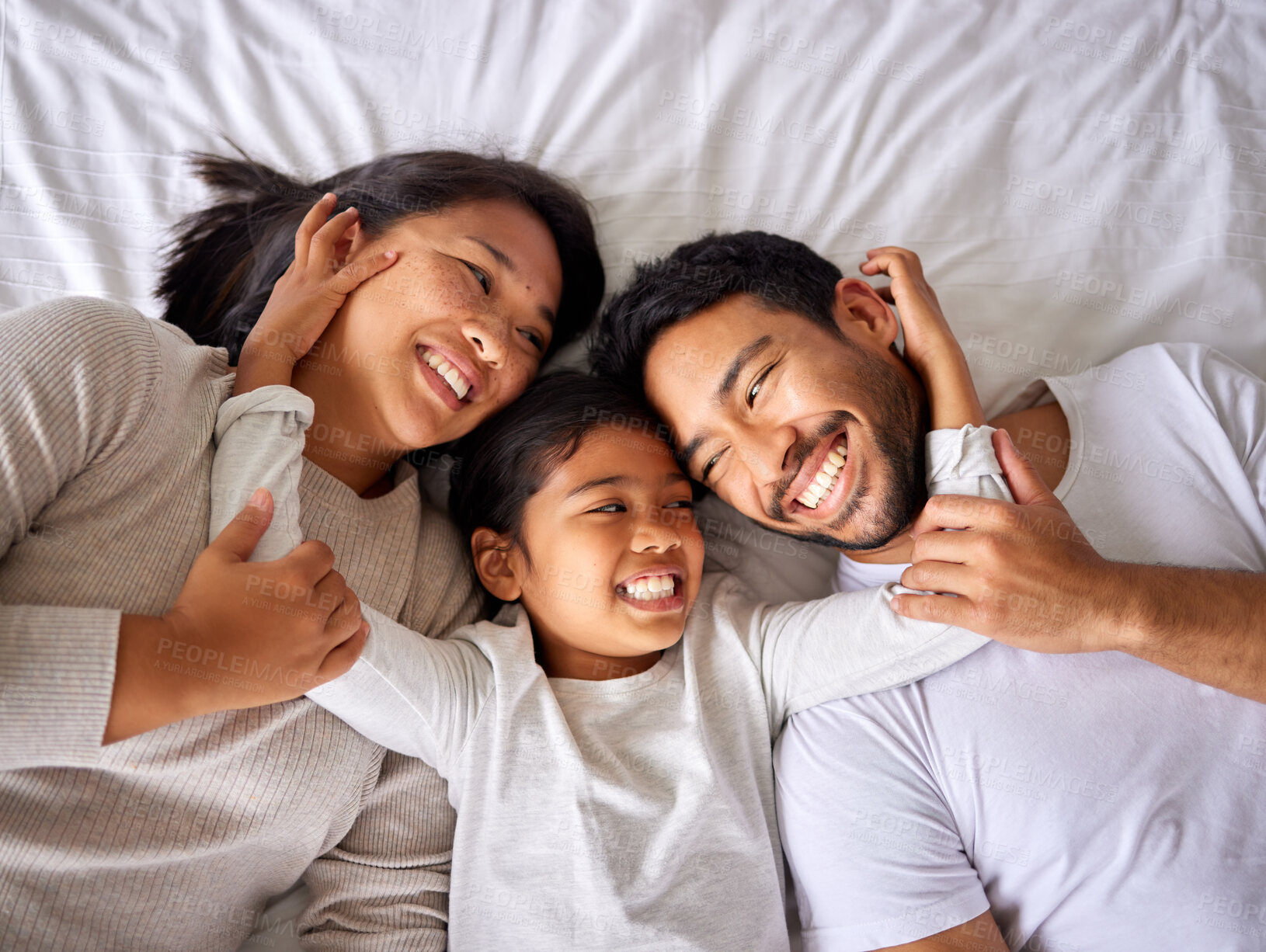 Buy stock photo Love, face and family in bed from above happy, smile and bonding in their home together. Hug, girl child and top view of parents with their daughter in a bedroom, relax and embracing indoors 