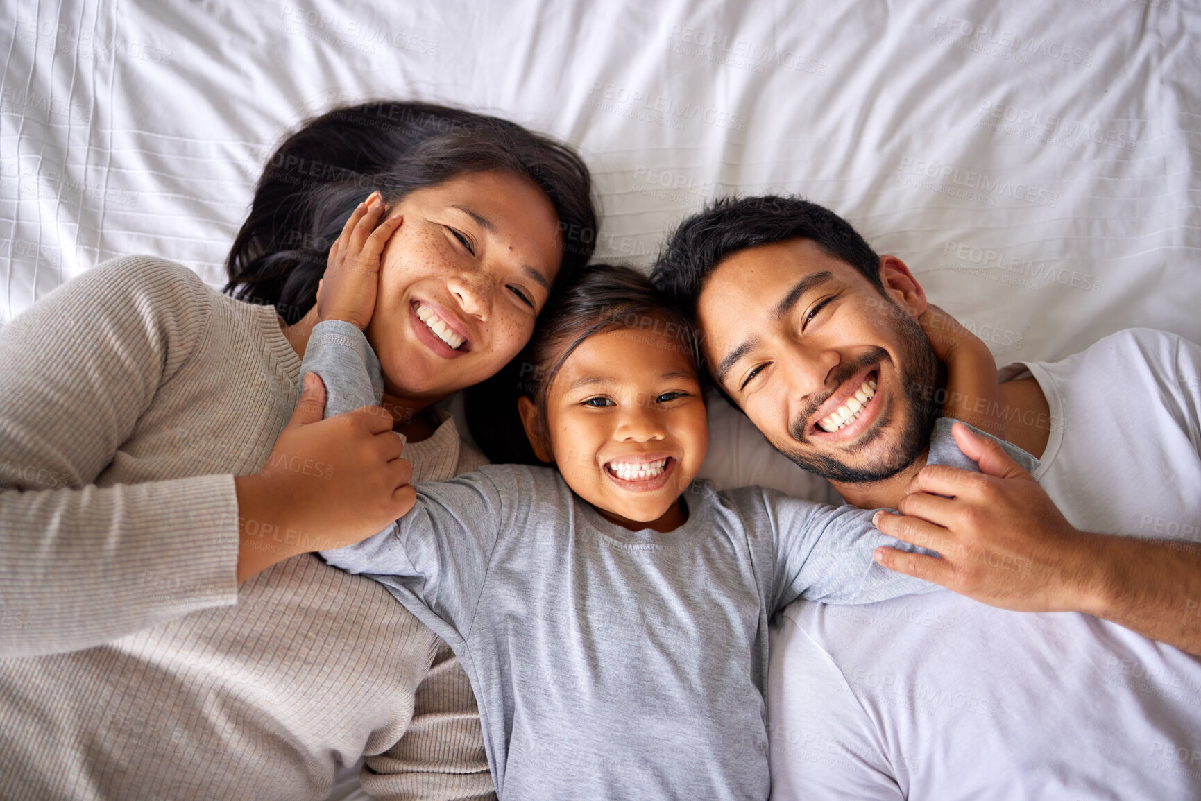Buy stock photo Portrait, love and family in bed from above happy, smile and bonding in their home together. Face, girl child and top view of parents with their daughter in a bedroom, relax and embracing indoors 