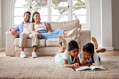 Young loving couple relaxing on the sofa while their little girls read a book on the floor at home