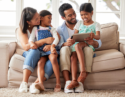 Buy stock photo Young smiling family of four streaming and using a digital tablet while relaxing on the sofa together at home