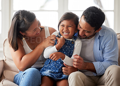 Positive family shot of a young ethnic couple smiling and laughing while bonding with their daughter on the sofa at home
