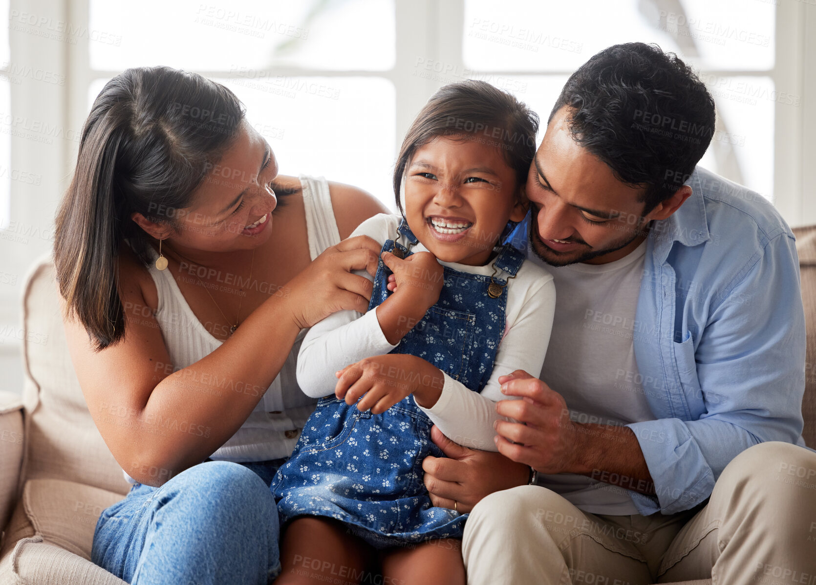 Buy stock photo Positive family shot of a young ethnic couple smiling and laughing while bonding with their daughter on the sofa at home