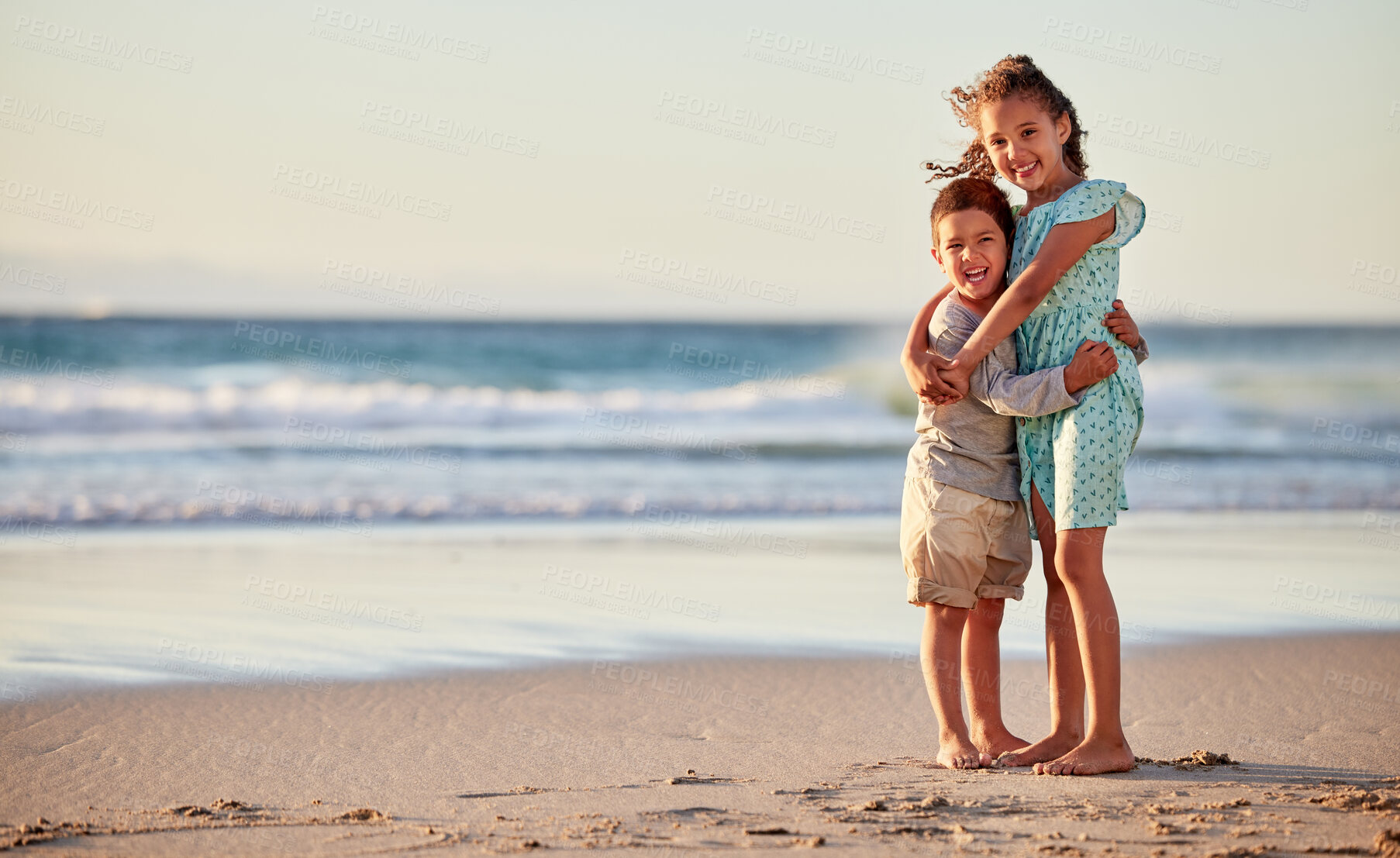 Buy stock photo Shot of an adorable little boy hugging his bigger sister while at the beach