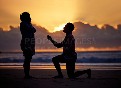 Buy stock photo Shot of a man proposing to his girlfriend during sunset at the beach
