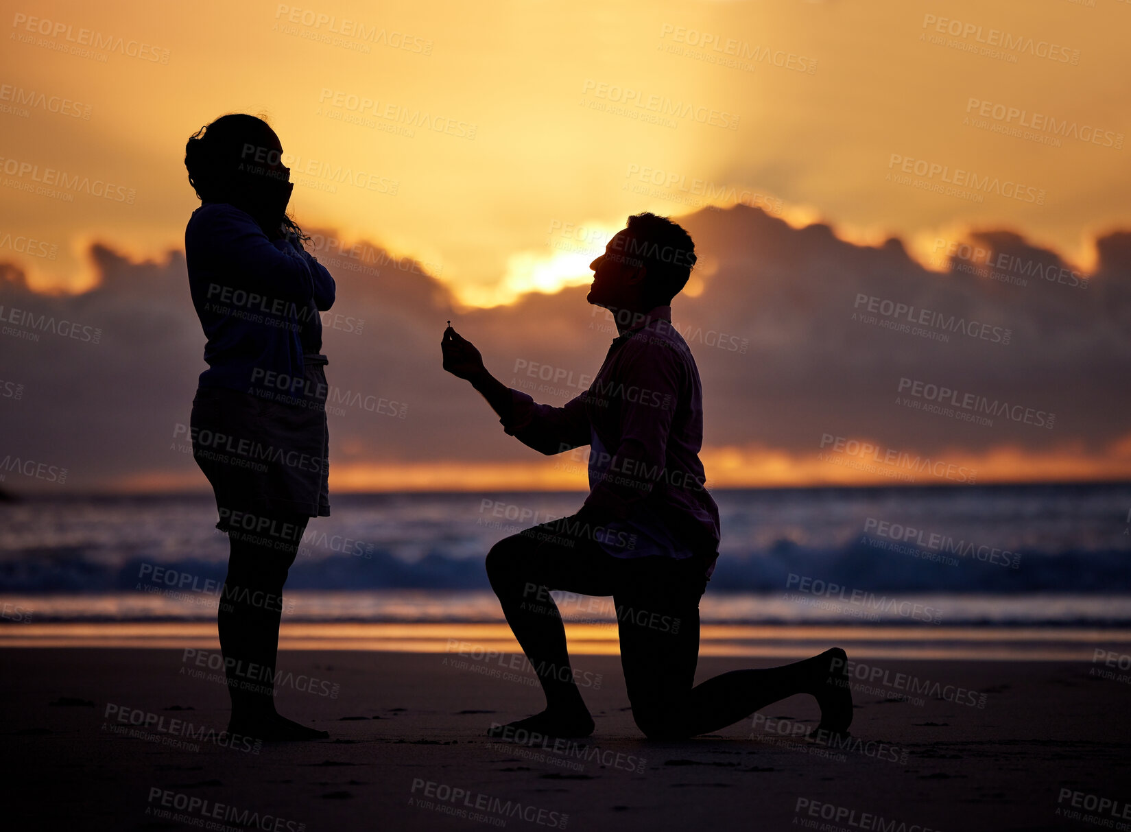 Buy stock photo Shot of a man proposing to his girlfriend during sunset at the beach