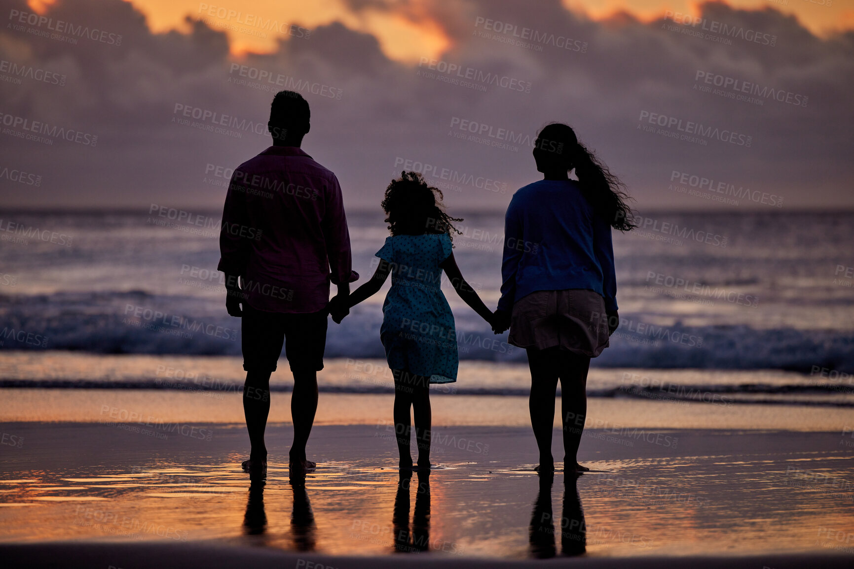Buy stock photo Silhouette shot of a couple and their daughter spending time at the beach during sunset