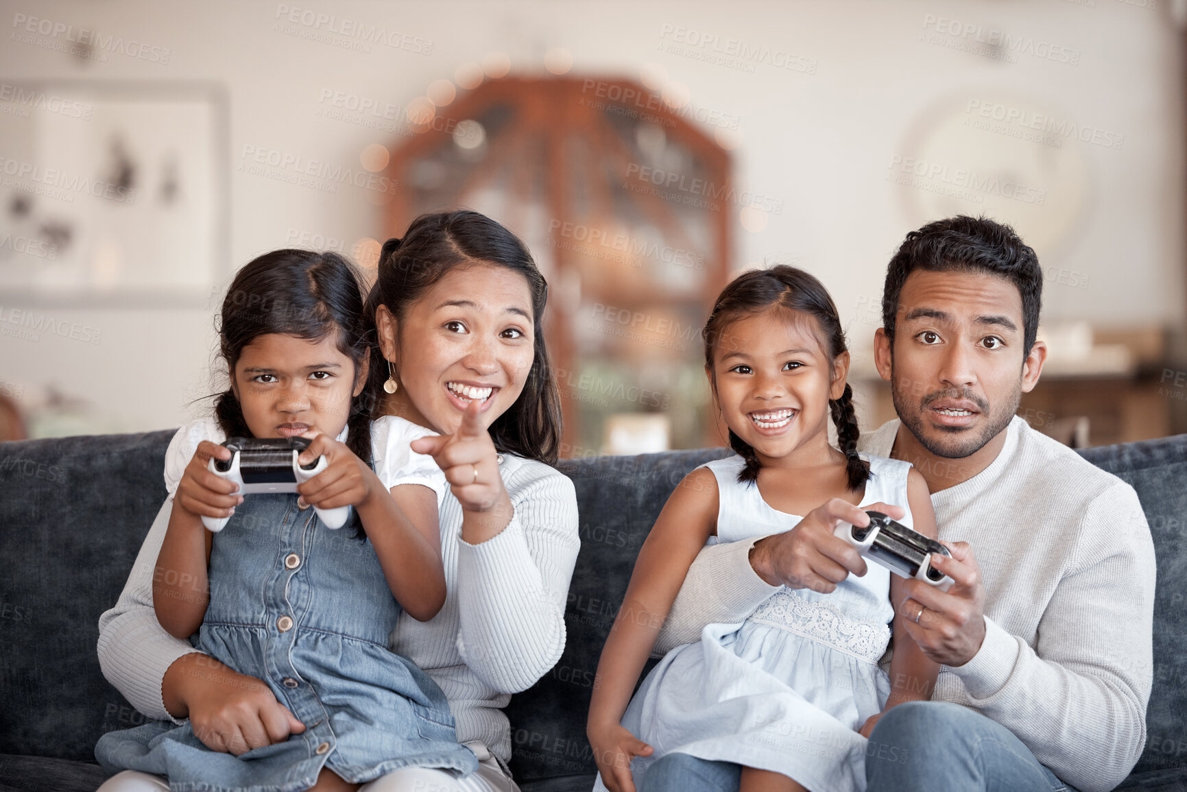 Buy stock photo Asian parents, children and video game on sofa with hug, point and strategy for contest with love. Father, mother and daughter with controller, competition and challenge at family home in Jakarta