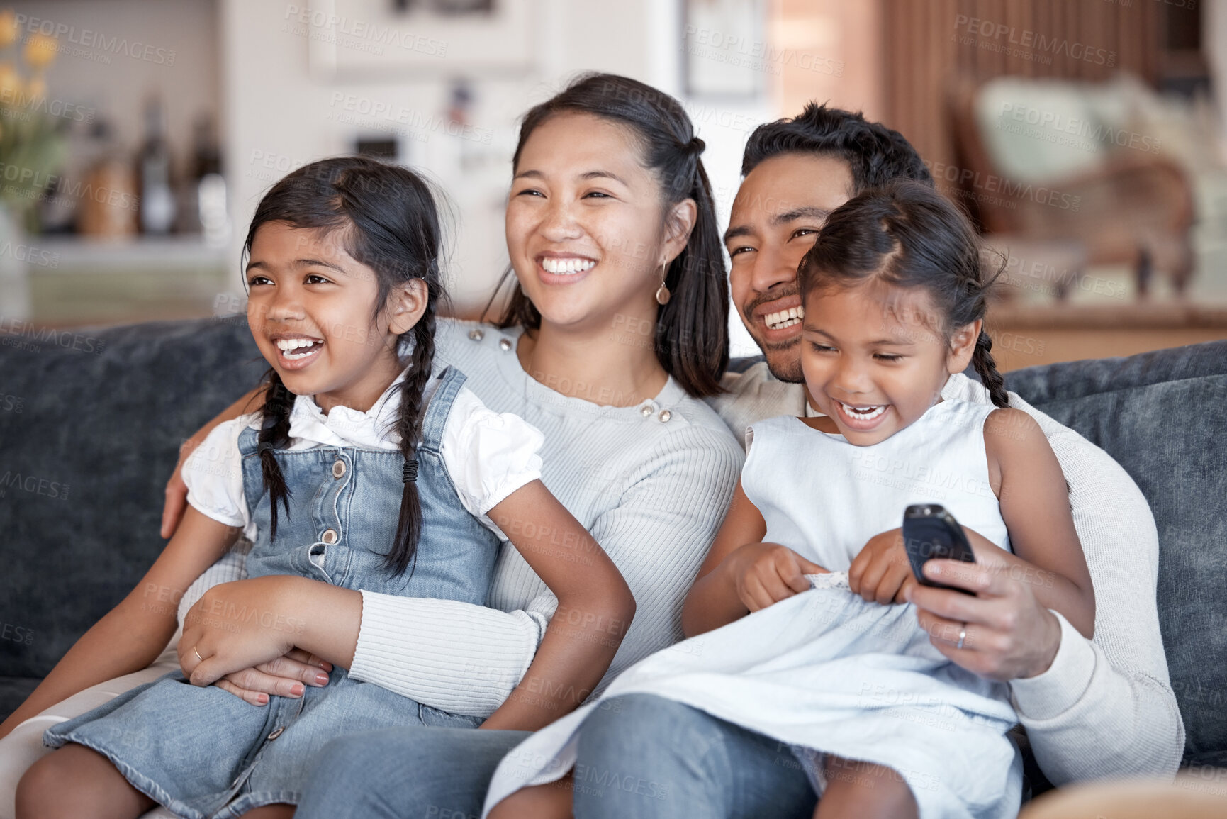 Buy stock photo Asian parents, children and watching tv on sofa with hug, care and love for comedy to relax in living room. Father, mother and daughter kids with funny movies for bonding at family house in Jakarta