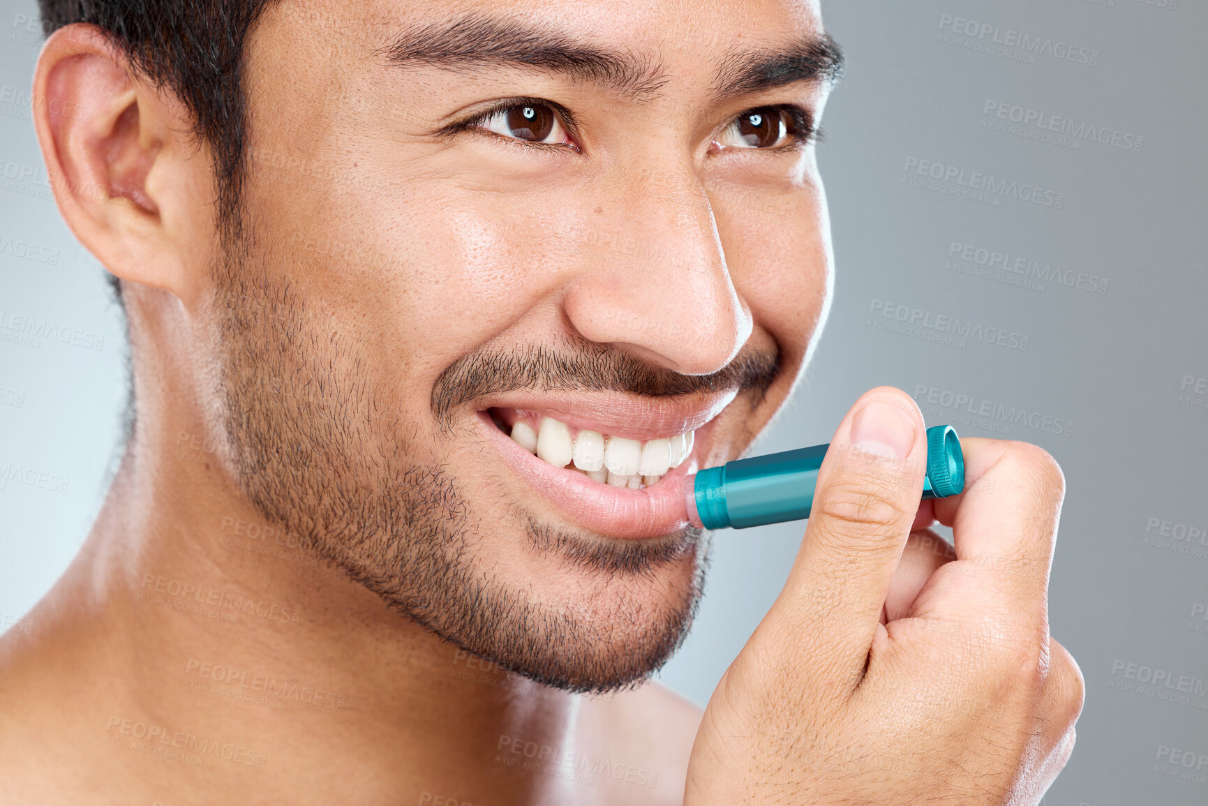 Buy stock photo Skincare, lip balm and man with cosmetics, smile and clear skin on grey studio background. Person, health and model with confidence, treatment and moisture with dermatology, wellness and grooming