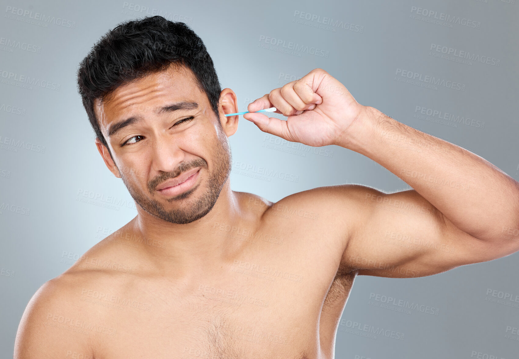 Buy stock photo Man, cotton bud and cleaning ear in studio for grooming, hygiene and morning routine. Male person, earbuds and wax removal on gray background for wellness, regret and unpleasant feeling for body care