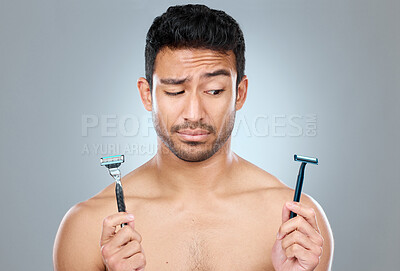 Buy stock photo Asian man, shaving and choice with razor blade for grooming, skincare or hair removal on a gray studio background. Handsome male person or young model with tools for decision, comparison or facial