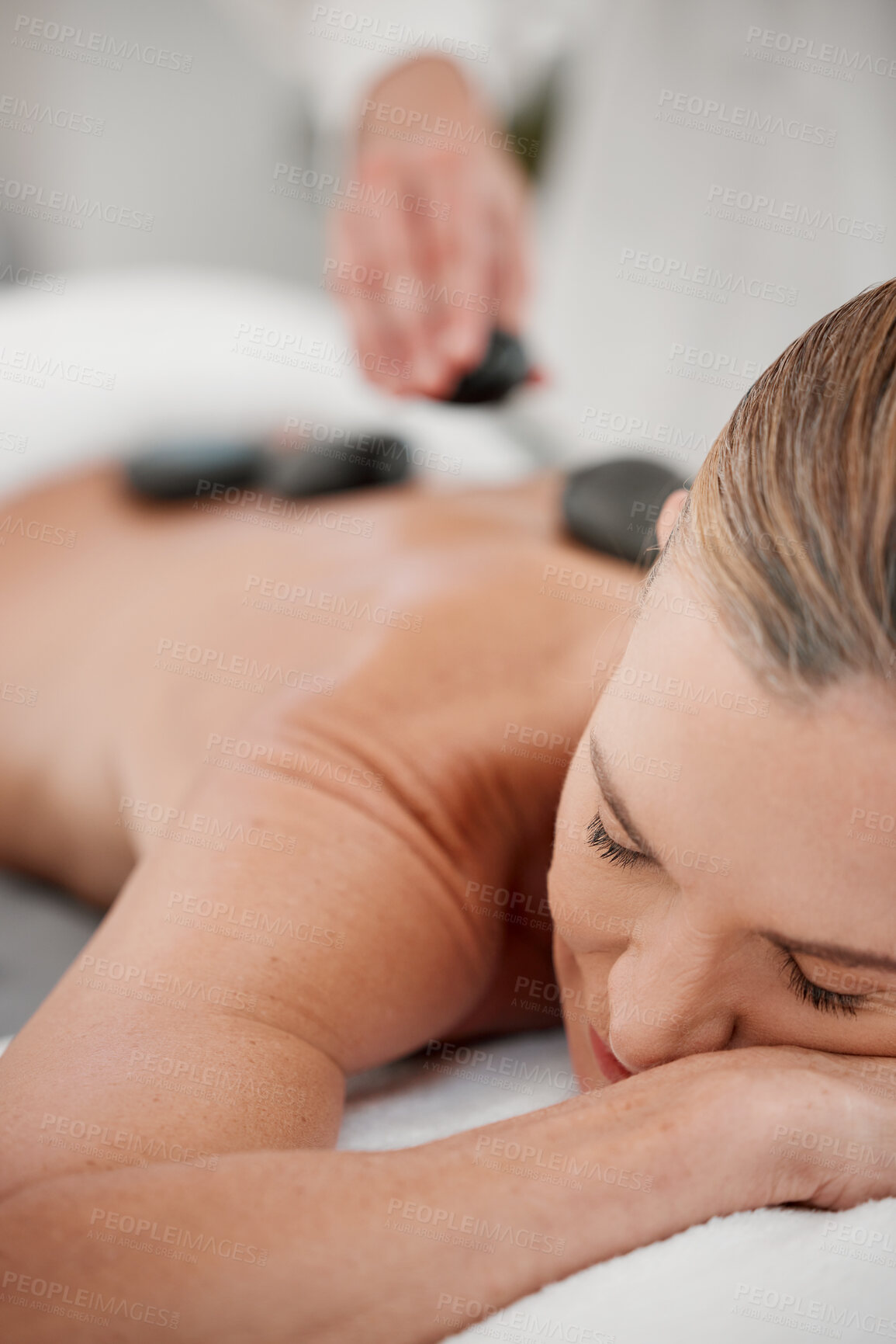 Buy stock photo Shot of a massage therapist placing hot stones onto a clients back during a treatment