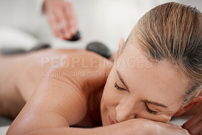 Buy stock photo Shot of a massage therapist placing hot stones onto a clients back during a treatment