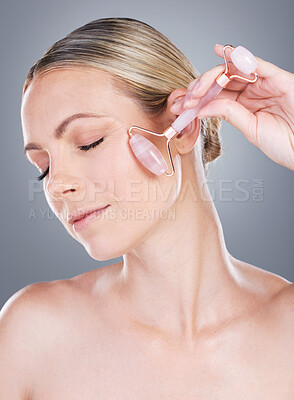 Buy stock photo Woman, relax and derma roller with rose quartz for skincare, anti aging or facial treatment on a gray studio background. Young female person or calm model for dermatology, beauty or skin wellness