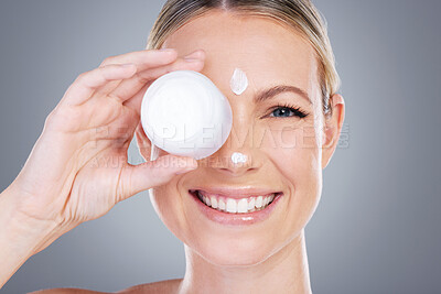 Buy stock photo Studio portrait of an attractive mature woman applying moisturiser on her face against a grey background