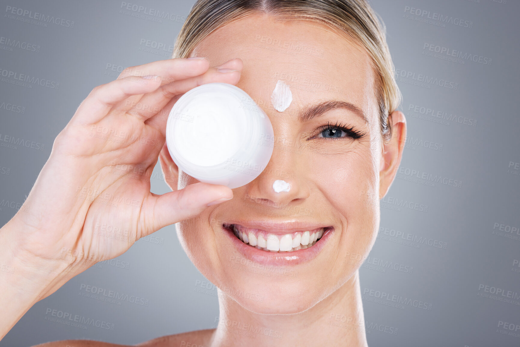 Buy stock photo Studio portrait of an attractive mature woman applying moisturiser on her face against a grey background