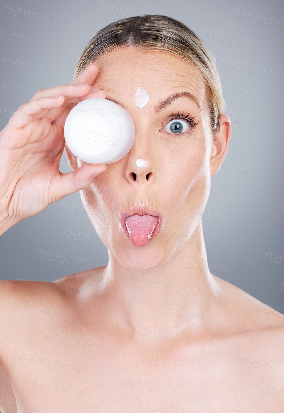 Buy stock photo Studio portrait of an attractive mature woman applying moisturiser on her face against a grey background