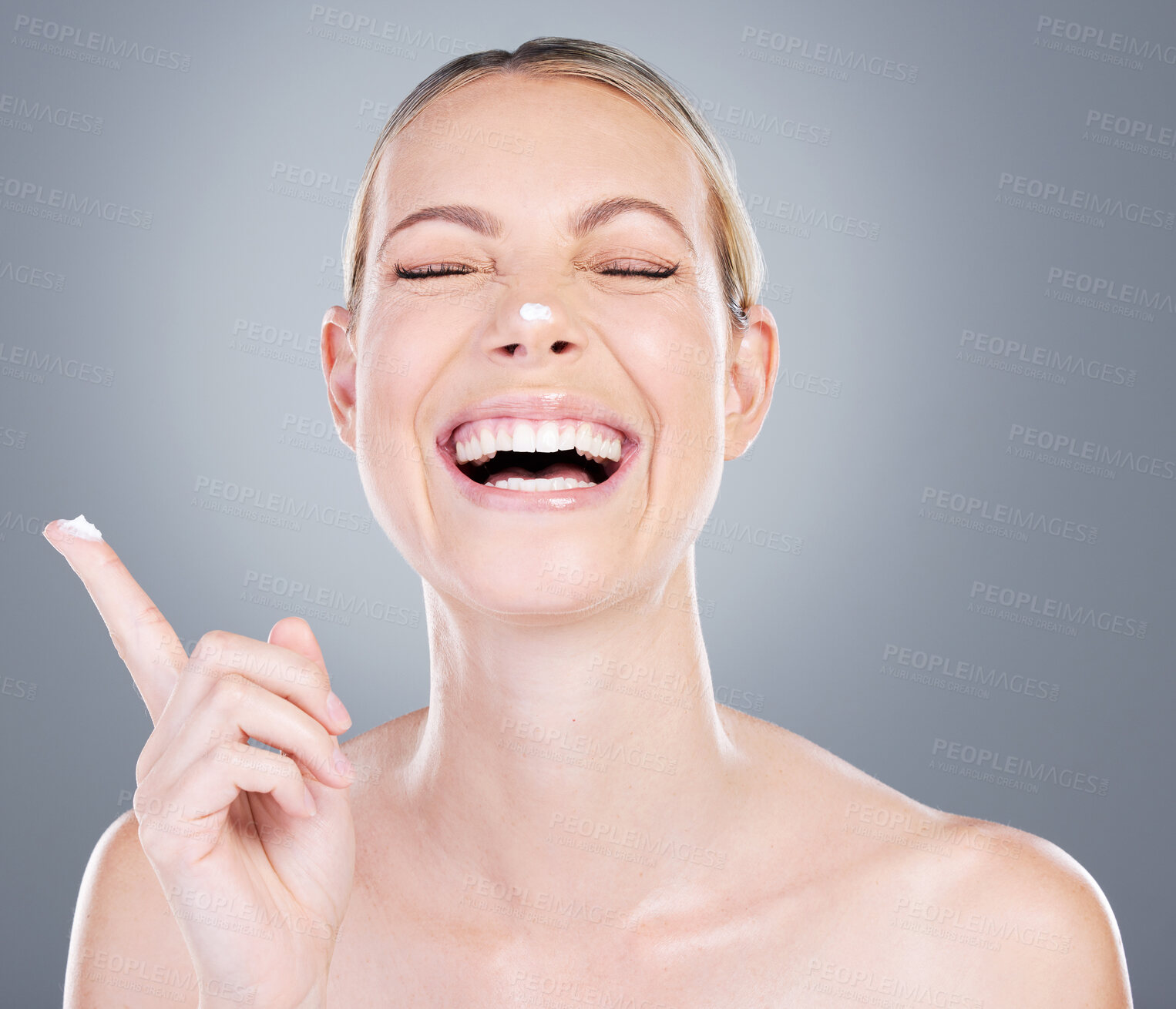 Buy stock photo Happy woman, skincare and laughing with lotion on nose for moisturizer on a gray studio background. Young female person or model with smile in satisfaction for face cream or anti aging treatment