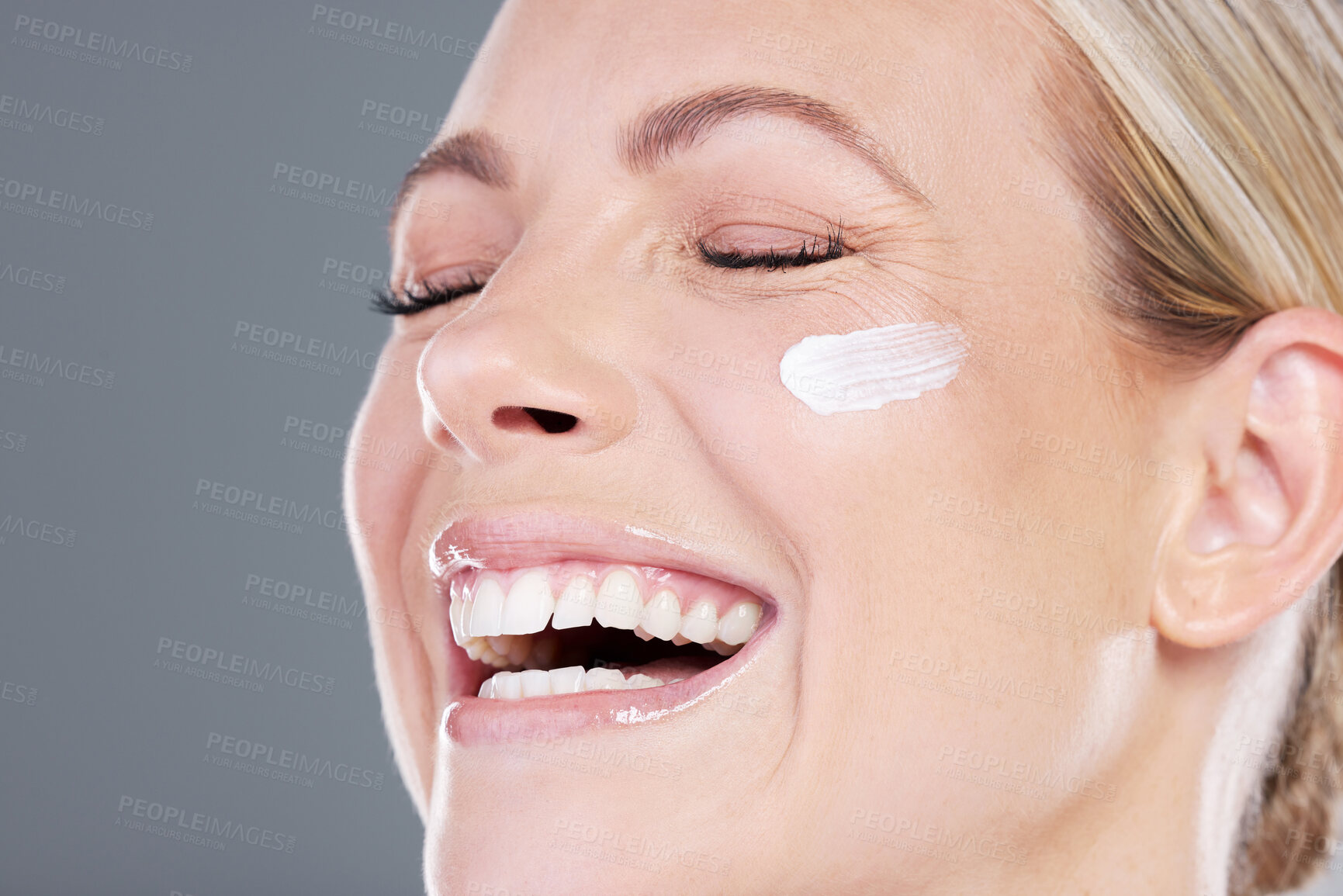 Buy stock photo Happy woman, skincare and cheek with moisturizer, lotion or face cream on a gray studio background. Young female person or model with smile in satisfaction or joy for anti aging or facial treatment