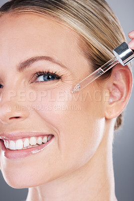 Buy stock photo Studio portrait of an attractive mature woman applying serum to her face against a grey background