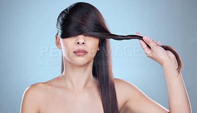 Buy stock photo Studio shot of a beautiful young woman playfully covering her eyes with her hair while posing against a blue background