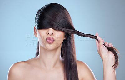 Buy stock photo Studio shot of a beautiful young woman playfully covering her eyes with her hair while posing against a blue background