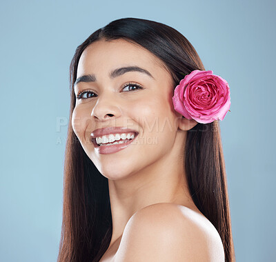 Buy stock photo Studio portrait of a beautiful young woman wearing a flower in her hair while posing against a blue background