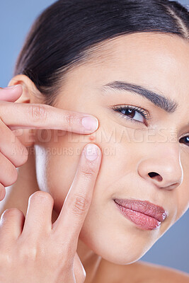 Buy stock photo Cropped shot of an attractive young woman posing alone against a blue background in the studio and picking pimples