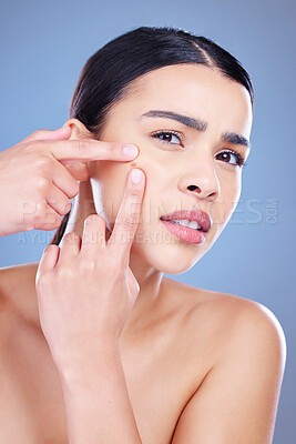 Buy stock photo Shot of an attractive young woman posing alone against a blue background in the studio and picking pimples