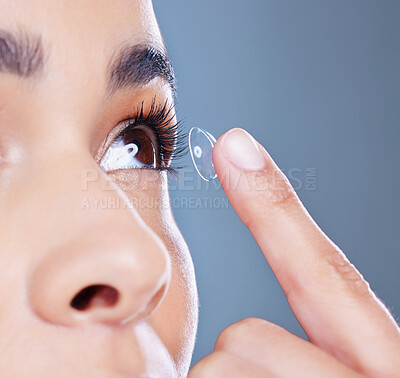 Buy stock photo Cropped shot of an unrecognisable woman posing against a blue studio background and putting a contact in her eye