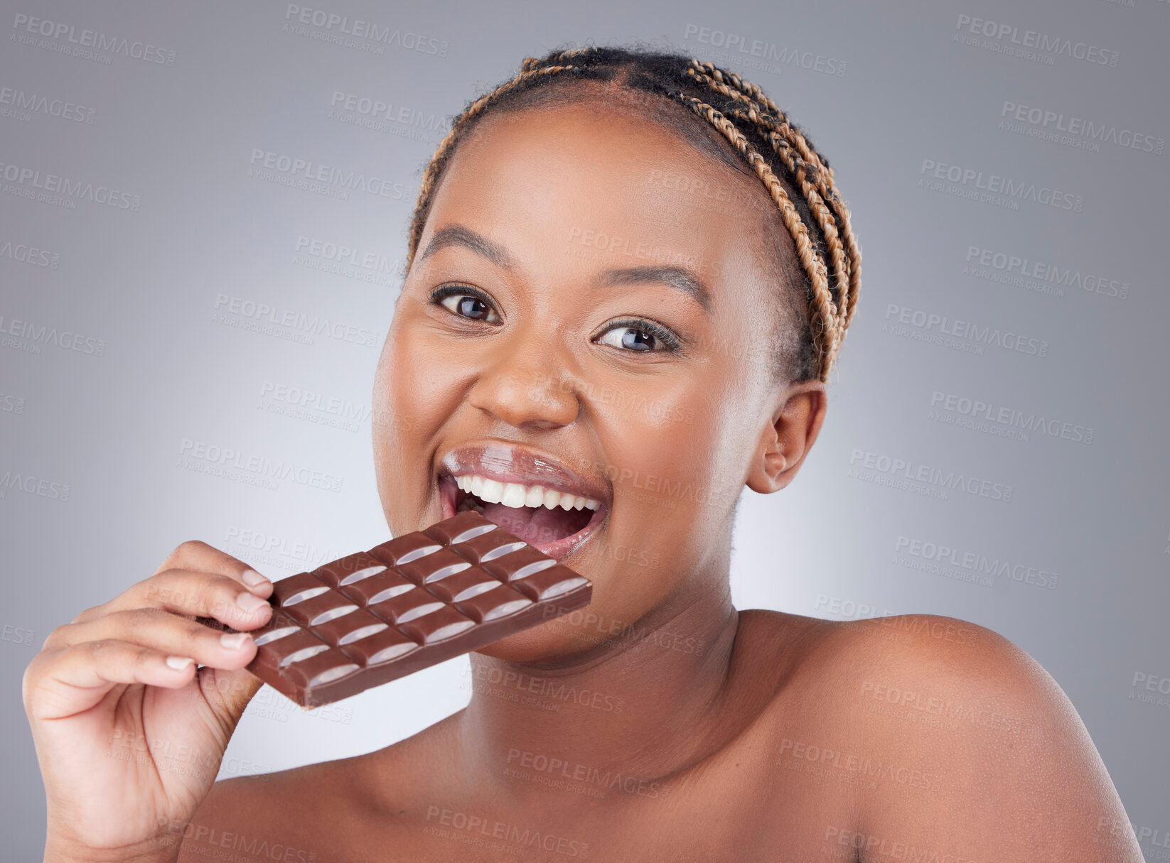 Buy stock photo Woman, portrait and eating a dark chocolate in studio with skincare, beauty and antioxidants. Model, black person and slab candy for cheat meal, sweet craving or wink for pms snack on gray background