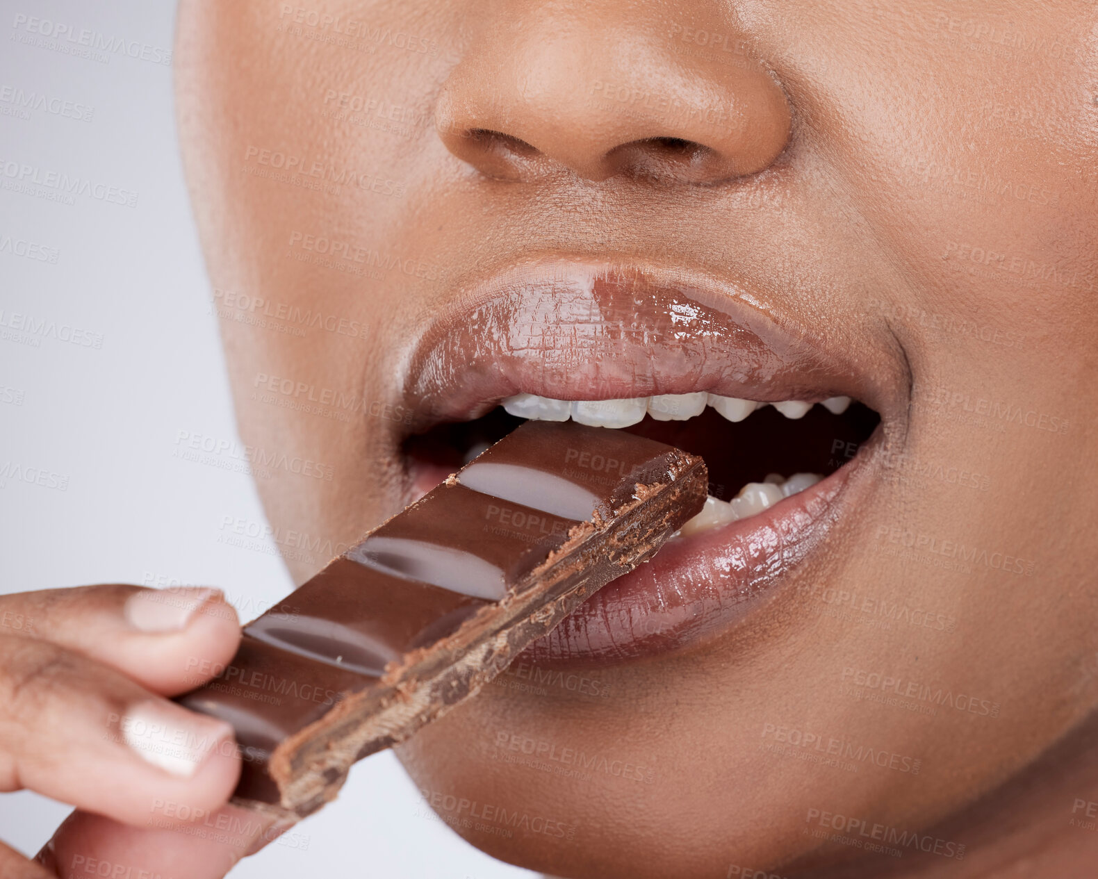 Buy stock photo Person, mouth and eating a chocolate bar in studio for dessert, sugar diet and sweet temptation with closeup. Model, slab candy and bite for cheat meal, cocoa craving and pms snack on gray background