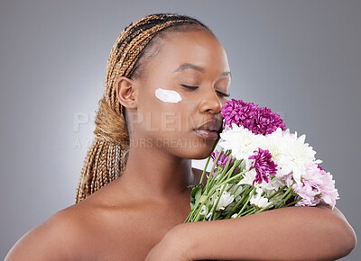 Buy stock photo Woman, face or lotion with flowers in studio for natural beauty, organic skincare or eco friendly sunscreen. Model, black person or serious with moisturizer treatment for skin glow on gray background