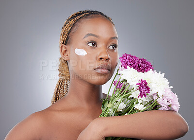 Buy stock photo Woman, face and moisturizer with flowers in studio for natural beauty, organic skincare or eco friendly sunscreen. Model, black person or serious with cream treatment for skin glow on gray background