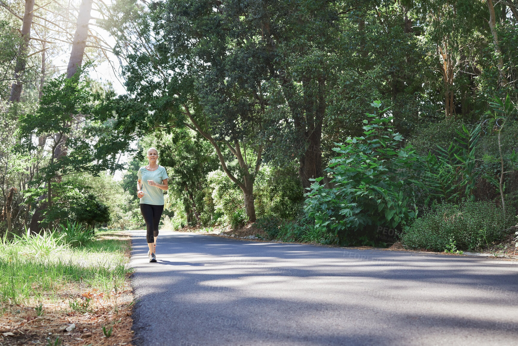 Buy stock photo Fitness, workout and a running senior woman on a road through a forest or park for cardio and endurance. Exercise, mockup and health with a mature female runner or athlete training outdoor in nature