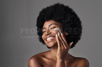 Buy stock photo Beauty, skin care and black woman with lotion on face, afro and cosmetics in studio on grey background. Natural skincare, collagen cream and African model with salon glow, dermatology and wellness.