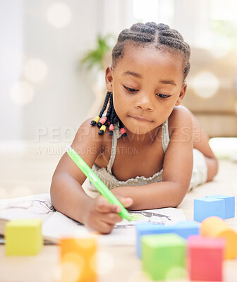 Buy stock photo Shot of an adorable little girl lying on the living room floor alone and colouring