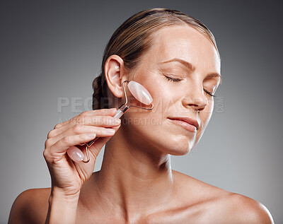 Beautiful mature woman posing with face roller in studio against a grey background