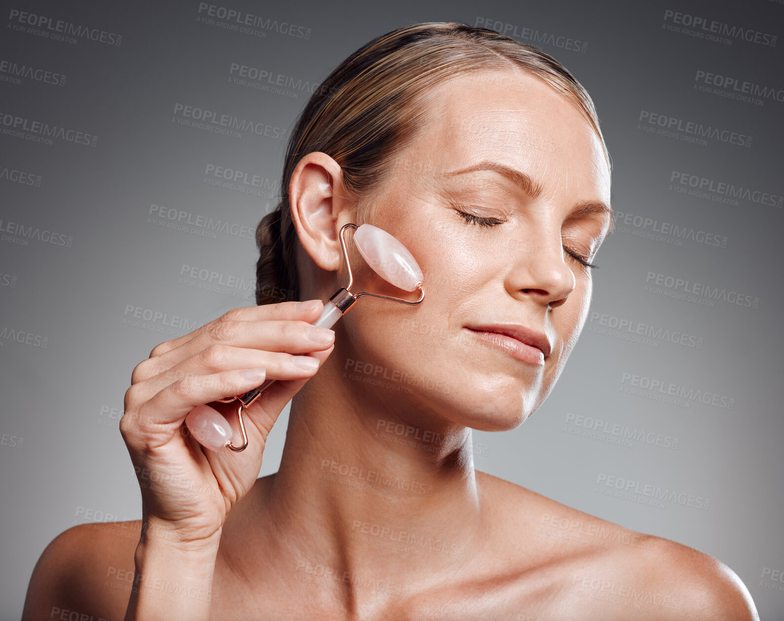 Buy stock photo Face roller, beauty and mature woman with skincare, cosmetics and shine on gray studio background. Person, mockup space or model with tool for smooth skin, grooming routine or aging treatment or glow