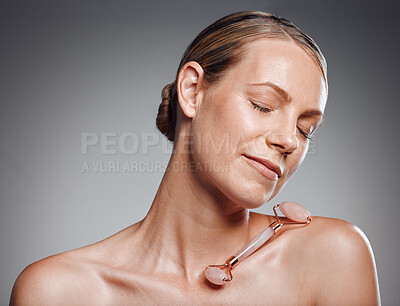 Beautiful mature woman posing with face roller in studio against a grey background