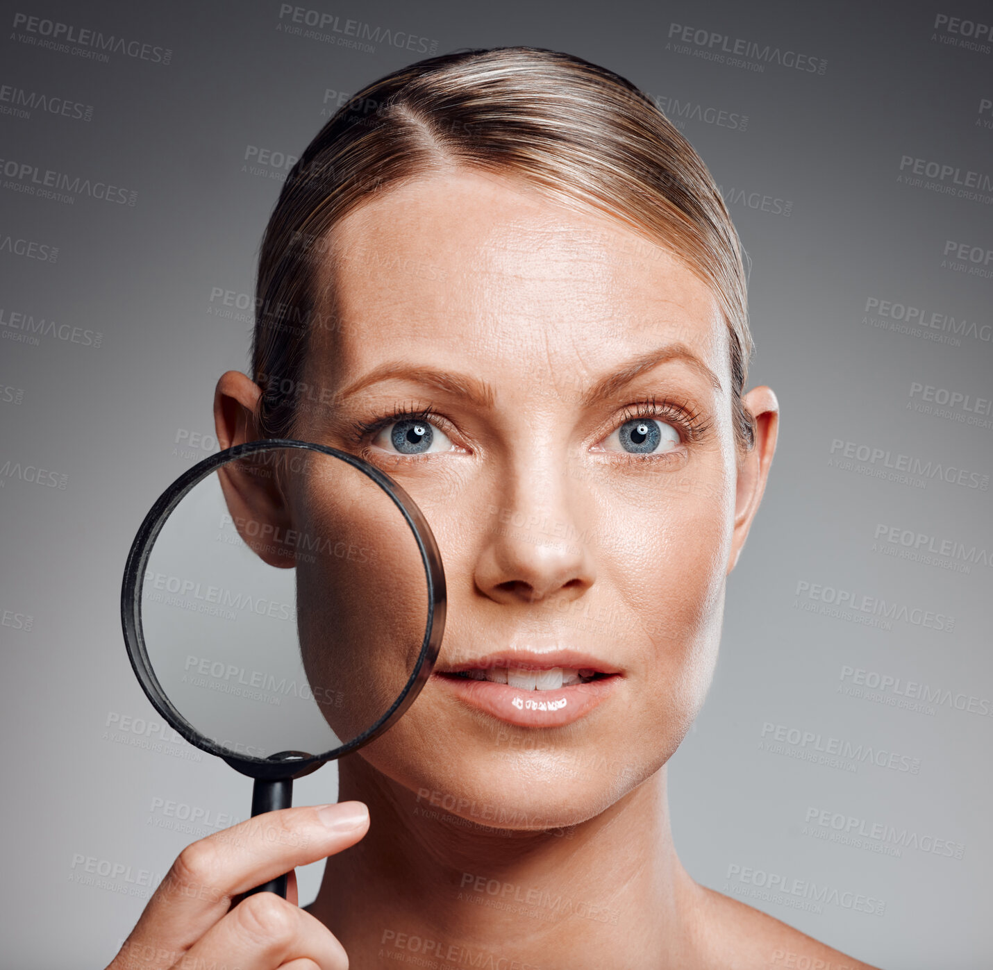 Buy stock photo Beautiful mature woman posing with magnifying glass in studio against a grey background