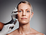 Beautiful mature woman getting botox injection in studio against a grey background