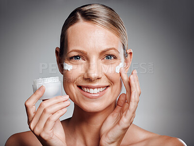 Beautiful mature woman posing with face lotion in studio against a grey background