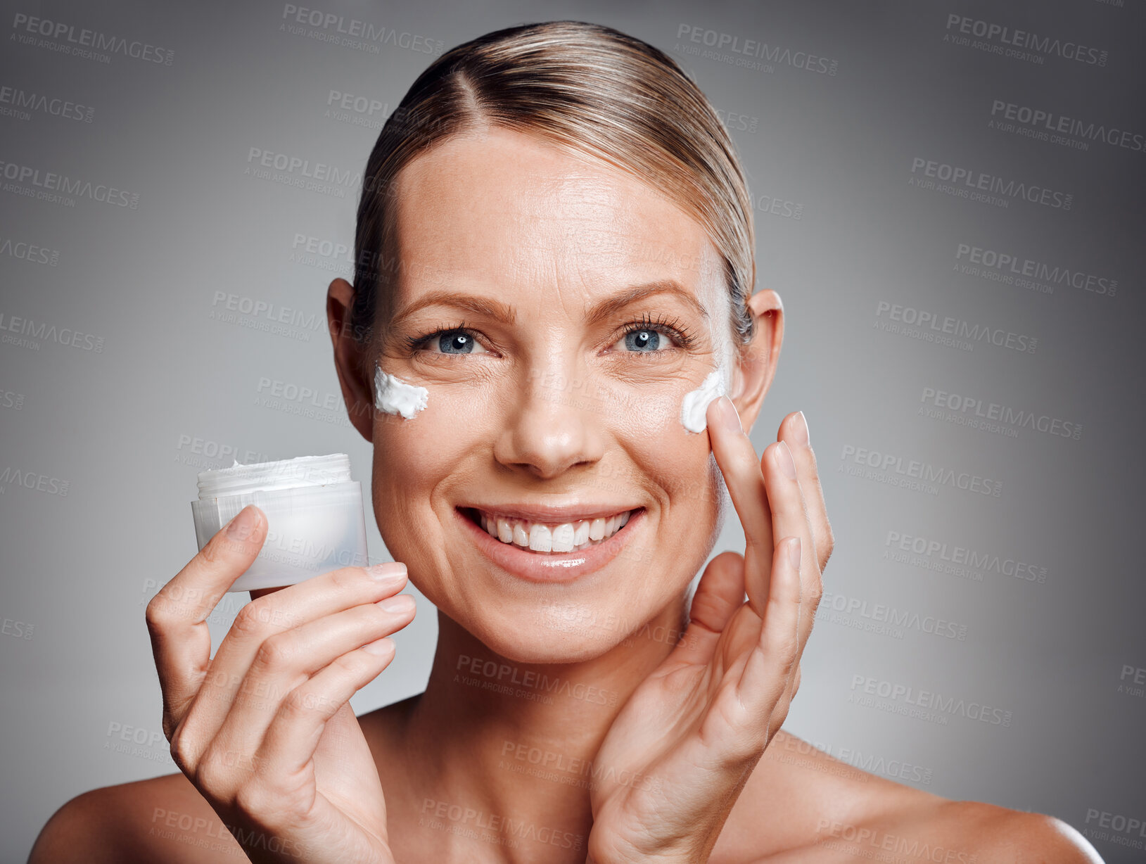 Buy stock photo Beautiful mature woman posing with face lotion in studio against a grey background
