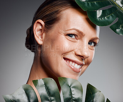 Beautiful mature woman posing with palm leaf in studio against a grey background
